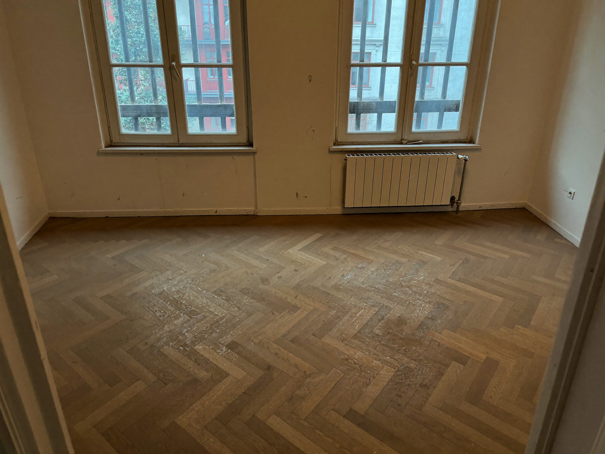Leere Wohnung mit stumpfem, fleckigem Parkett vor der Endreinigung